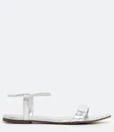 Sandalia plana plateada con puntera fina, tira elástica en el tobillo y tira fija sobre los dedos.