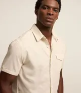 Camisa de hombre de manga corta color marrón, confeccionada en lino y algodón. Presenta cuello clásico, botonadura frontal, bolsillo en el pecho y mangas con botón para enrollar.