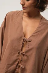 Blusa marrón de corte crop, escote en V y mangas largas anchas. Cierre frontal con lazos.