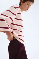 Remera de manga tres cuartos con cuello redondo, hombros caídos y corte holgado. Presenta un patrón de rayas horizontales en tonos rosa pálido, blanco y granate.