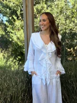 Camisa de lino azul marino con volados en cascada a lo largo del frente y en los puños de las mangas largas. Presenta un escote en V con un botón de nácar visible.