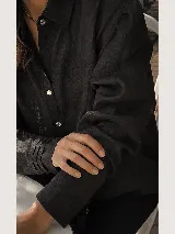 Camisa de lino color negro con cuello clásico, cierre frontal de botones y detalle de tablitas horizontales en el frente. Posee mangas largas con puños simples.