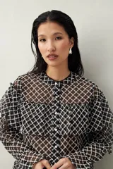 Camisa blanca de encaje bordado con diseño semitransparente, silueta fluida y mangas largas. Se destaca por los volados en el frente y hombros.