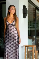 Vestido largo con estampado tie-dye en tonos violeta y fucsia, escote en V con detalles bordados dorados, cut-outs laterales bajo el busto y tirantes finos que se cruzan y atan en la espalda.