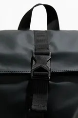Mochila en tejido revestido color negro con cierre enrollable, hebilla central y bolsillo vertical con cierre en un lateral. Cuenta con correas acolchadas y espalda acolchada.