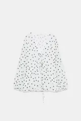 Top de crepe blanco con estampado de lunares negros, escote en V y cierre frontal con finas lazadas. Presenta mangas largas abullonadas con puños elásticos y bajo redondeado.