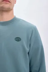Sudadera verde de cuello redondo y manga larga, con puños y cintura acanalados. Estampado de un escorpión en el pecho.