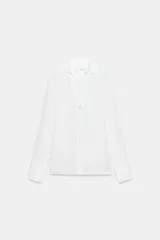 Camisa de cuello solapa y escote en pico, con manga larga y cierre frontal mediante botones. Presenta un diseño fluido con bajo asimétrico y aberturas laterales.