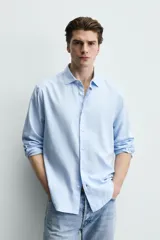 Camisa de corte regular fit confeccionada en tejido de algodón con textura twill. Presenta cuello italiano, manga larga con puños abotonados y cierre frontal de botones.