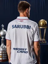 Camiseta de fútbol Umbro del Club Nacional de Football, modelo Home 2026. Diseño blanco con tejido jacquard que presenta un patrón sutil de copas históricas. Incluye cuello en V con detalles en azul y rojo, logo de Umbro, escudo del club y sponsor Antel en el frente.