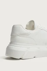 Zapatilla de estilo urbano con suela de plataforma voluminosa y diseño irregular. Presenta un diseño de paneles en la parte superior y cierre mediante cordones.