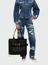 Bolso tote de lona color negro de Marc Jacobs, modelo The Cargo Canvas Large Tote Bag, con múltiples bolsillos externos con solapa y cierre, asas superiores de cuero y texto impreso contrastante en el frente.