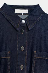 Camisa de denim color azul oscuro, con cuello solapa, manga larga y corte cropped. Presenta dos bolsillos de plastrón con tapa en el frente y cierre frontal con botones metálicos.