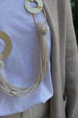 Collar largo de diseño artesanal compuesto por múltiples cordones de algodón en color crudo, entrelazados con aros y eslabones metálicos en tono dorado mate.