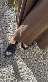 Sandalias planas con punta cuadrada, base negra y capellada de cuero marrón con textura trenzada.