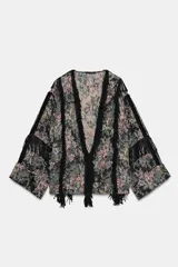 Kimono de tejido jacquard con estampado floral multicolor sobre fondo oscuro. Presenta un diseño abierto con aplicaciones de flecos negros a contraste en los bordes frontales y en las mangas. Posee mangas tres cuartos con terminación en vuelta y aberturas laterales en el bajo.