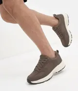 Championes deportivos Renner de color marrón, con diseño robusto y capellada que combina material sintético liso y paneles de malla respirable. Cuentan con cordones tono sobre tono, suela gruesa de goma en color blanco y detalles negros en la parte inferior.
