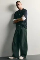 Pantalón barrel fit de mezclilla color verde militar, con efecto lavado, cinco bolsillos, cierre frontal con cremallera y botón, y detalle de pinzas en las rodillas.