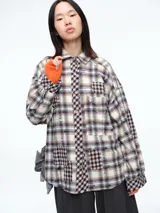 Sobrecamisa de corte oversize con diseño patchwork de cuadros en tonos beige, marrón y negro. Presenta efecto desgastado, cierre frontal con botones y bolsillo en el pecho.