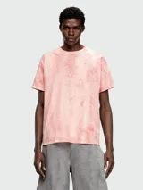 Remera de manga corta, cuello redondo y calce holgado, color rosa pálido con un efecto de teñido o estampado que simula grietas o craquelado en tonos más oscuros de rosa/naranja.