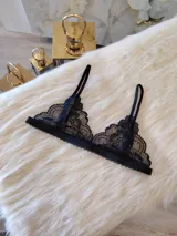 Bralette de encaje negro estilo triángulo, con breteles regulables y cierre frontal con broche de gancho.
