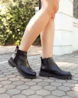 Botinetas de cuero negro con suela track dentada. Presentan un diseño de caña baja con paneles laterales elásticos y cierre lateral, combinando texturas de cuero liso y texturizado.