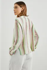 Blusa de lino a rayas verticales de color blanco, naranja, verde y marrón, con cuello camisero, mangas largas con puños y lazos ajustables en el escote.