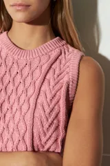 Chaleco de tejido de punto color marrón oscuro, con diseño de ochos y rombos en relieve. Tiene cuello redondo y es sin mangas.