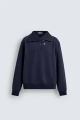 Sudadera de calce relajado color azul marino, con cuello alto y cierre frontal mediante alamares metálicos. Presenta manga larga y terminaciones en rib en puños y cintura.