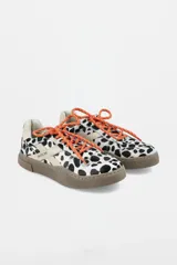 Zapatillas urbanas de cuero con estampado animal print tipo dálmata, suela de goma color marrón y cordones de color naranja vibrante.