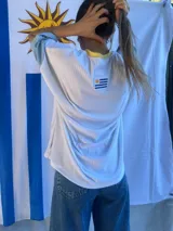 Remera de corte oversize confeccionada en tejido de punto acanalado color celeste, con mangas cortas en color amarillo y detalle de parche bordado con la bandera de Uruguay en la parte superior de la espalda.