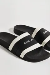 Sandalias tipo chinelas de diseño bicolor en negro y blanco, con banda ancha frontal que incluye el logo de la marca en relieve.