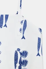 Top de escote recto con tirantes finos ajustables, estampado con motivos marinos de peces y conchas en color azul sobre fondo blanco. Presenta detalle de botones decorativos en el frente y aberturas en el bajo.