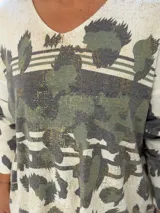 Sweater de punto con cuello en V y mangas largas, de diseño holgado. Presenta un estampado abstracto en tonos verdes con detalles metalizados en color dorado sobre una base de color crema.