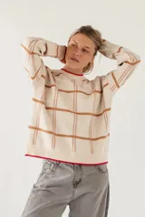 Sweater de punto con diseño de cuadros en tonos beige y marrón, cuello redondo y detalles de borde en color rojo en el cuello y el ruedo.