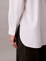 Camisa de corte relaxed confeccionada en popelina de algodón con elastano. Presenta cuello de punta clásico, cierre frontal con botones, mangas largas y un bolsillo en el pecho con el monograma CK bordado en relieve.