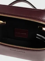 Cartera tipo vanity bag Marc Jacobs modelo The Pop J Marc E/W, color bordó, de diseño estructurado con cierre perimetral de cremallera dorada y herraje metálico distintivo de la marca en la parte frontal. Cuenta con asa superior corta.
