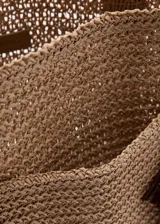 Bolso tipo tote color marrón, confeccionado en tejido de fibra natural de papel, con asas largas de hombro y detalle de charm colgante con flecos.