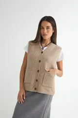Chaleco tejido de punto en color beige, con cuello en V, cierre frontal de botones oscuros y dos bolsillos delanteros aplicados.