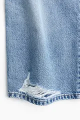 Jean de corte wide leg con diseño de cinco bolsillos, confeccionado en denim de algodón rígido. Presenta un lavado claro con efecto desgastado y un detalle de rotura en la rodilla izquierda. Cuenta con cintura clásica, cierre de botón y bragueta.