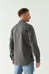 Camisa de gabardina color gris oscuro, con corte slim, manga larga, cuello clásico, cartera abotonada y dos bolsillos frontales con solapa.
