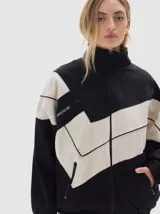 Campera de jean con diseño color block en negro y beige, corte oversized, cuello alto, cierre frontal y bolsillos laterales con cierre. Presenta detalles de costuras visibles y logo de la marca estampado en el pecho.