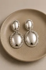 Aros colgantes de diseño ovalado en dos niveles, con acabado plateado pulido y borde texturizado con pequeñas esferas.