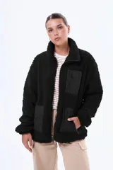 Campera de sherpa negra con cuello alto y cierre frontal completo. Presenta paneles de tela técnica en los bolsillos laterales y un bolsillo superior con cierre. Diseño de corte holgado y textura afelpada.
