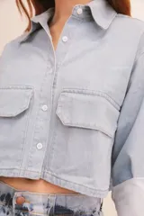 Camisa de denim azul con cuello clásico, cierre frontal con botones, mangas largas con puños abotonados y dos bolsillos tipo cargo en el pecho.