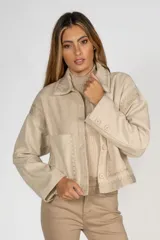 Sobrecamisa color beige con cuello camisero, botones frontales y detalles de bordado calado en el cuello, hombros, mangas y bajo. Tiene un bolsillo de parche en el pecho.