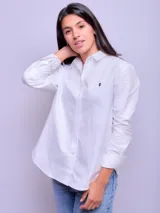 Camisa de corte suelto y diseño clásico, confeccionada en algodón. Presenta cuello camisero, cierre frontal con botones y mangas largas con puños abotonados. Incluye un pequeño bordado en el pecho.