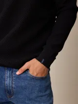 Sweater de punto color negro, con cuello alto y cierre frontal parcial tipo medio cierre. Presenta textura en el tejido y logo bordado en el pecho.