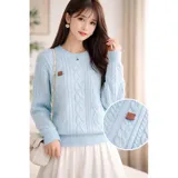 Sweater de punto color crema con diseño de trenzas y rombos, cuello redondo y mangas largas. Presenta un pequeño aplique decorativo en el pecho.