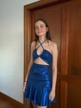 Vestido corto con estampado de rayas horizontales en tonos grises y negros. Diseño con escote halter que se ata al cuello, abertura central en el busto y falda corta con volado.